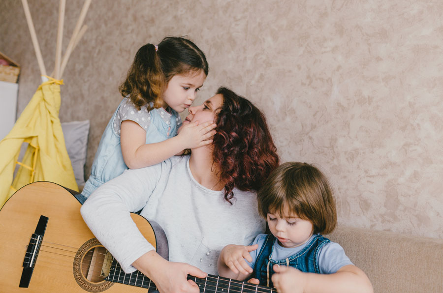 Eine glückliche Mama mit ihrer zwei Töchter spielt Gitarre.