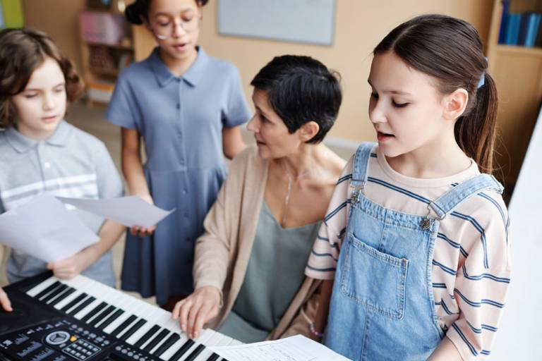 Kinder singen im Gesangsunterricht, die Lehrerin begleitet sie am Klavier