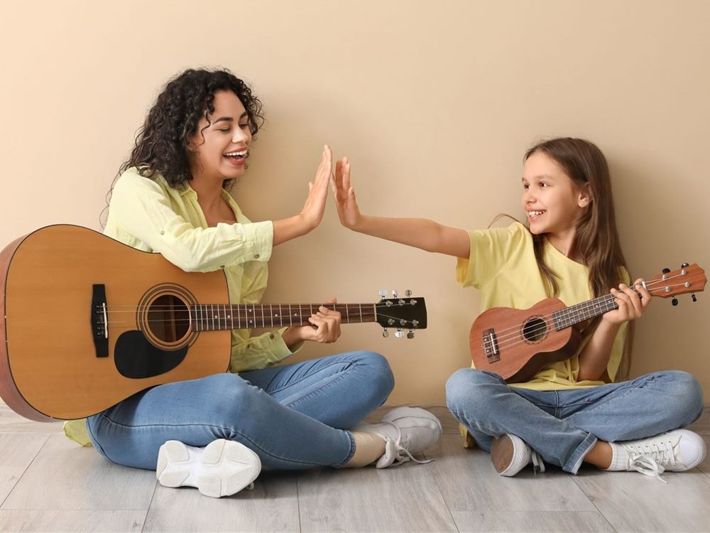 Mutter und Tochter spielen gemeinsam Gitarre und Ukulele und klatschen ab