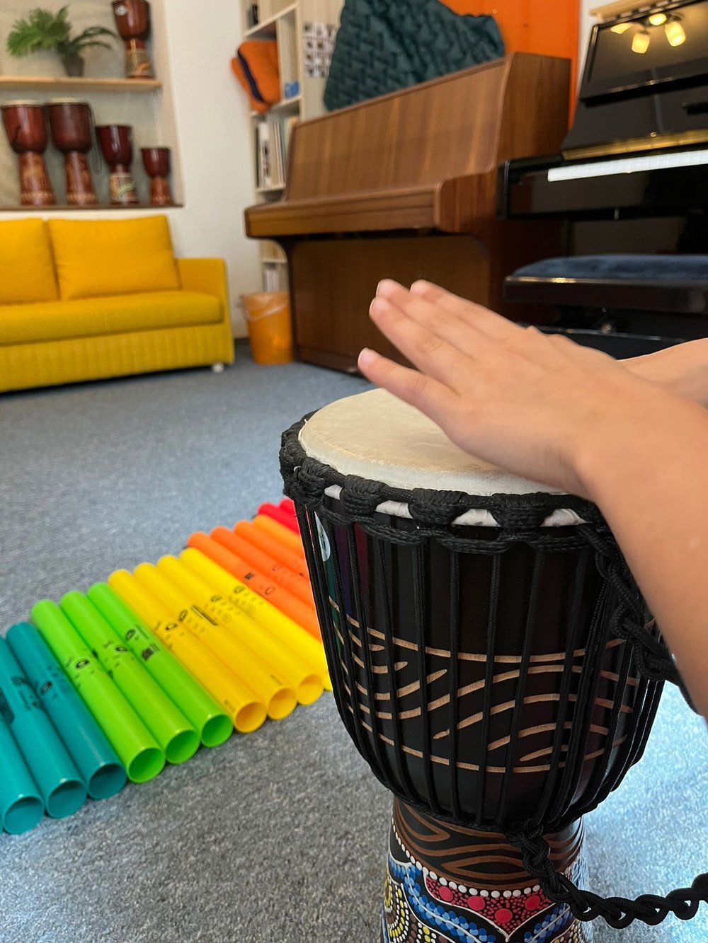 Kinderhand auf einer Trommel, dahinter bunte Klangröhren im Früherziehungsraum von Einfach Musikalisch